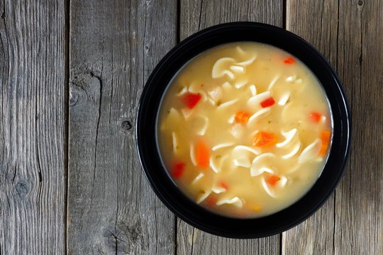 Traditional chicken noodle soup in a black bowl, above view on a rustic wood background