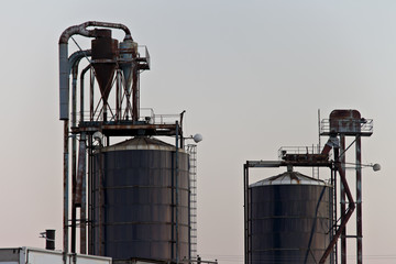 Old, rusted industrial style storage bins surrounded by crisp white sky.