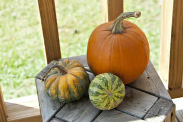 Trio of colorful pumpkins on wood stool.