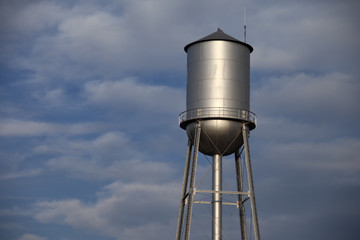 Tall silver water tower with cloudy blue sky background