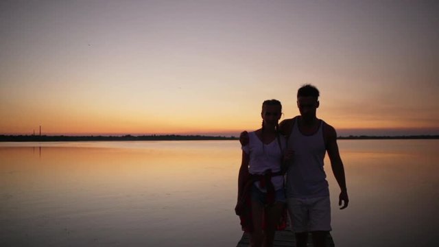 Young beautiful couple embracing walking on pier at sunrise Slow motion