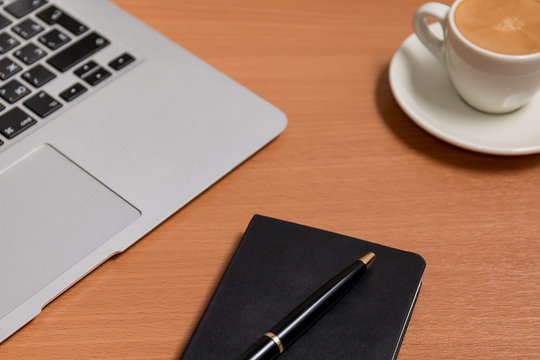 Workspace with pen on the notebook and notebook's keyboard and the cup of coffee on the background