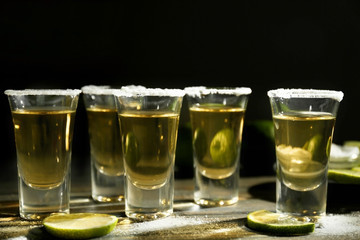 Gold tequila shots with lime and salt on wooden table