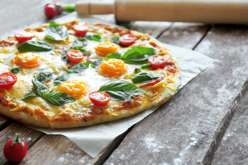 Margarita pizza with basil leaves and egg on wooden table closeup