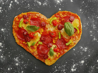 Tasty heart shaped pizza on black flour powdered table