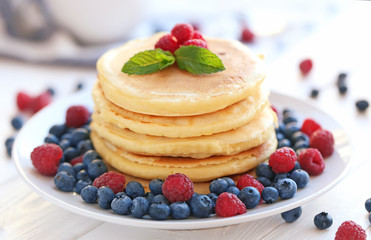 Plate with tasty pancakes and berries on wooden table