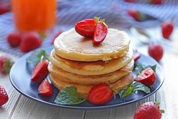 Plate with tasty pancakes and strawberries on wooden table