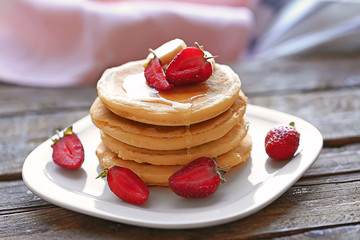 Plate with tasty pancakes and strawberries on wooden table, close up view
