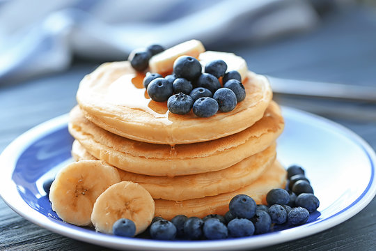 Plate with tasty pancakes, banana slices and berries on wooden table, close up view
