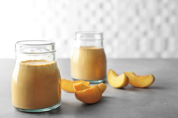 Mason jars with tasty smoothie and peach on table