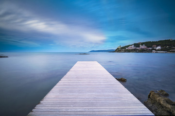 Fototapeta na wymiar Castiglioncello bay wooden pier, rocks and sea on sunset. Italy
