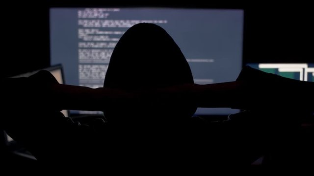 Hacker in hood cracking code using computers in dark room