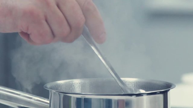 Metal pot on the stove. The chef mixes the contents of the pan using Tablespoon. Cooking of restaurant dishes. Saucepan with steam. The steam comes from the pan on the stove. The steam from cooking.