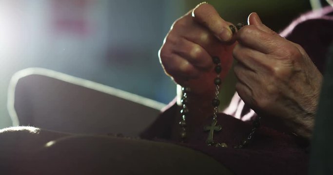 the hand of an elderly lady says a prayer by touching a rosary in the tradition of his religion