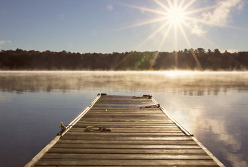 Cottage Dock  over looking the clam lake water on a misty morning with the sun shine - obrazy, fototapety, plakaty