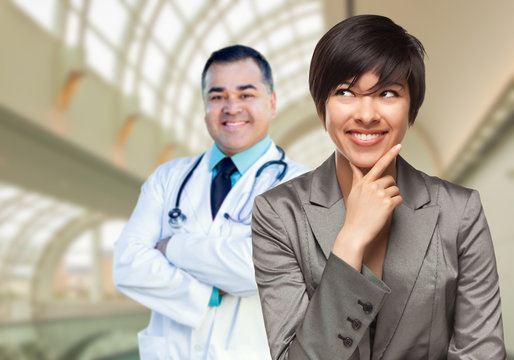 Happy Mixed Race Woman Looking To The Side As Hispanic Male Doctor Stands Behind Her Inside Hospital.