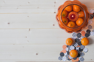 Light wooden background  with Halloween decoration: clementines , glass pumpkin and a garland. Copy space. 