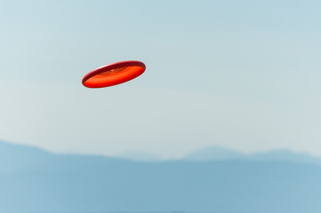 Frisbee flying through the air with a view of the mountains in the distance - obrazy, fototapety, plakaty