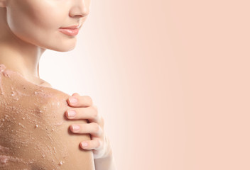 Young woman applying scrub on shoulder against color background. Skin care concept.