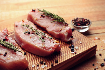 Raw steaks with herbs and spices on wooden cutting board