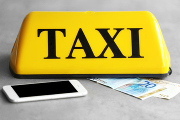 Yellow taxi roof sign with phone and Euro banknotes on gray background, closeup