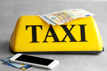 Yellow taxi roof sign with phone, credit cards and Euro banknotes on gray background, closeup