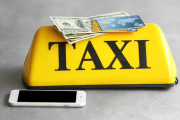 Yellow taxi roof sign with phone, credit cards and American dollars on gray background, closeup