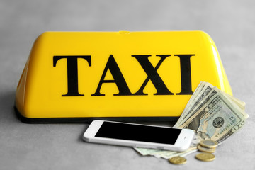 Yellow taxi roof sign with phone and money on gray background, closeup