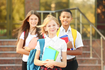 Fototapeta na wymiar Cheerful teenagers with backpacks and notebooks on school entrance background