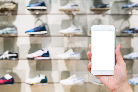 Hand hold mobile phone with sport shoes on shelves in the shoes