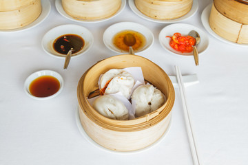 Dim sum food Steamed lava bun in bamboo basket at restaurant with soy sauce, sweet sauce, chili sauce and chopsticks.