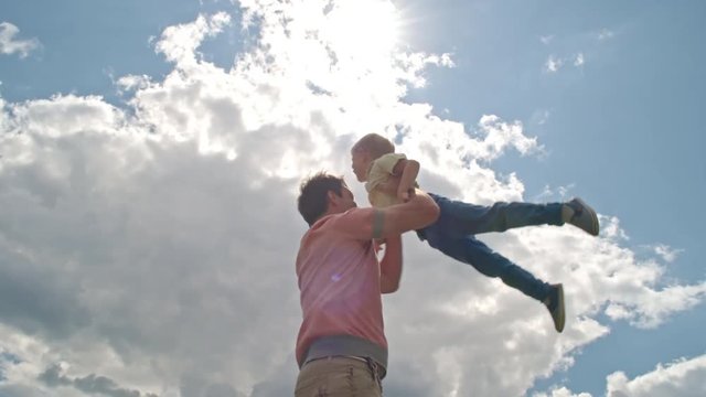 Low angle view of man holding his little son and spinning him around while playing outdoors