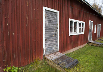 A wall of an old barn. Red shed walls with grey doors and white window frames.