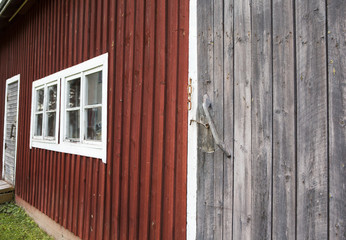 A wall of an old barn. Red shed walls with grey doors and white window frames.