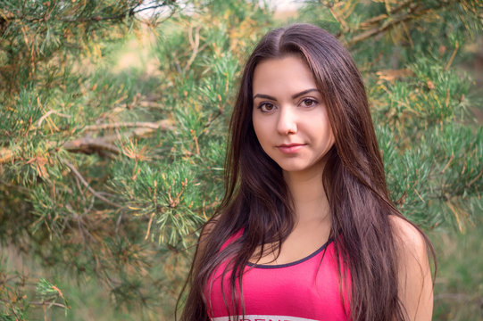 Young beautiful brunette model posing in the sports image of the park against the backdrop trees