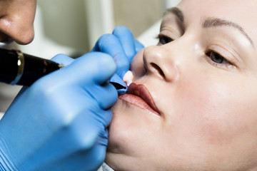 Cosmetologist applying permanent make-up. Young beautiful woman having cosmetic tattoo on her lips. Healthy Spa