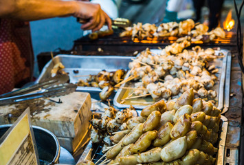 Fototapeta na wymiar Evening street food in Bangkok, Thailand : Grilled squid on gridiron in evening street market, Squid barbecue in Thai street food market