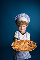 Little boy chef with a pizza on a blue background in studio