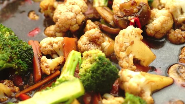 Cooking healthy vegetable stir fry with broccoli, cauliflower, carrots in soy sauce marinade, slow motion