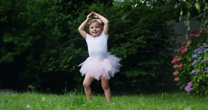 little girl tries to take the first dancer steps in a garden dressed as a little dancer happy dancer funny . concept first steps and happy childhood nature . little funny children. cinema camera