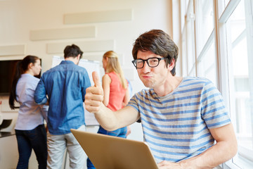 Student am Laptop Computer hält Daumen hoch