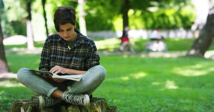 young student boy in the checked shirt use the tablet in a park in a moment of relaxation and enjoys his day