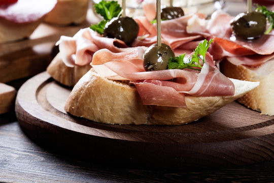 Spanish tapas with slices jamon serrano, salami, olives and cheese cubes on a wooden table