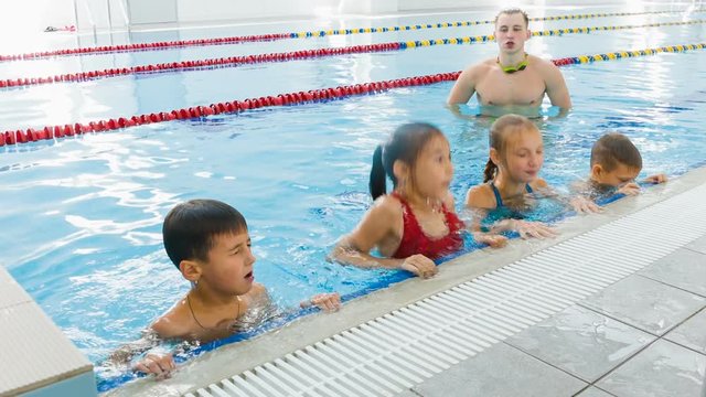 Instructor or coach and group of children doing exercises in swimming pool