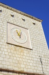 The Krk Town Council Hall clock at Vale Market place on island Krk, Croatia. A rook medieval structure with a 24h clock with latin numbers and yellow pointers.