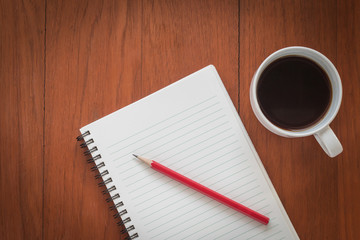 Note book with pencil and a cup of coffee on wood table