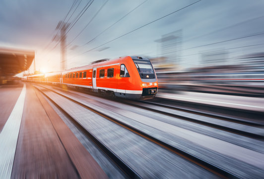 Fototapeta Beautiful railway station with modern high speed red commuter train with motion blur effect at colorful sunset. Railroad with sunlight. Vintage toning. Travel. Train
