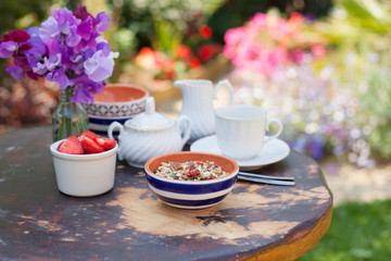 Breakfast in the garden: gluten, grain free cereals on the weathered wooden table, with white cup and saucer and sweet peas on the back, selective focus