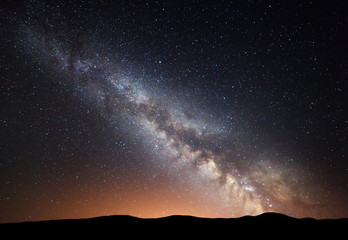 Night landscape with amazing Milky Way and yellow light at mountains. Starry sky with hills at...