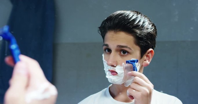 A young boy shaves his beard for the first time and looks in the mirror smug in slow motion